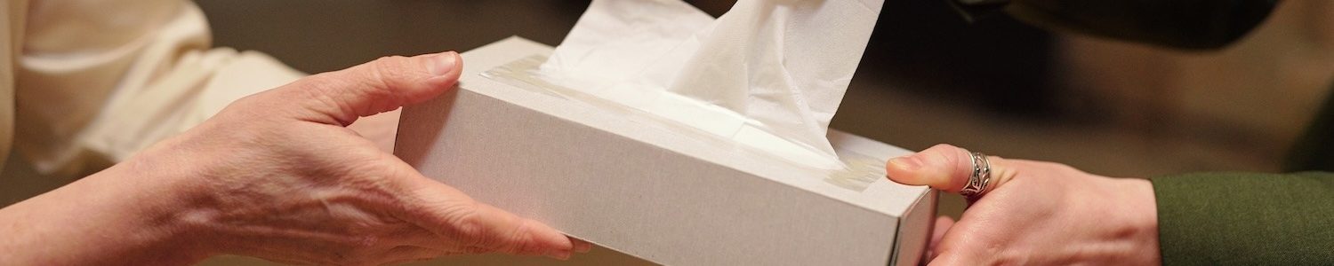 Young female taking paper handkerchief out of box held by psychologist